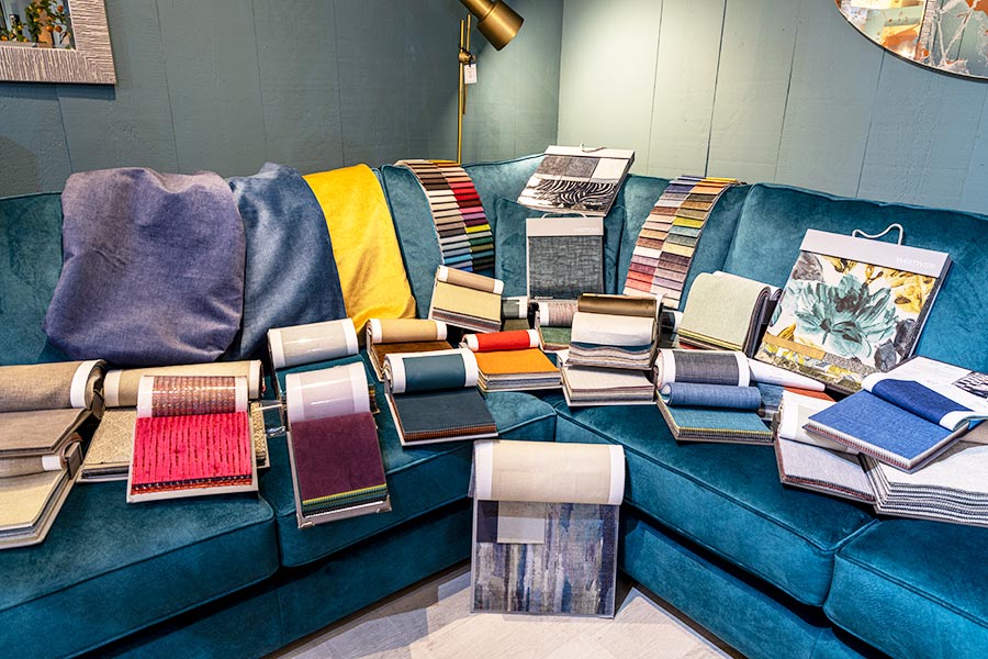 A large selection of luxury sofa fabrics displayed on a blue corner sofa at New England Home Interiors